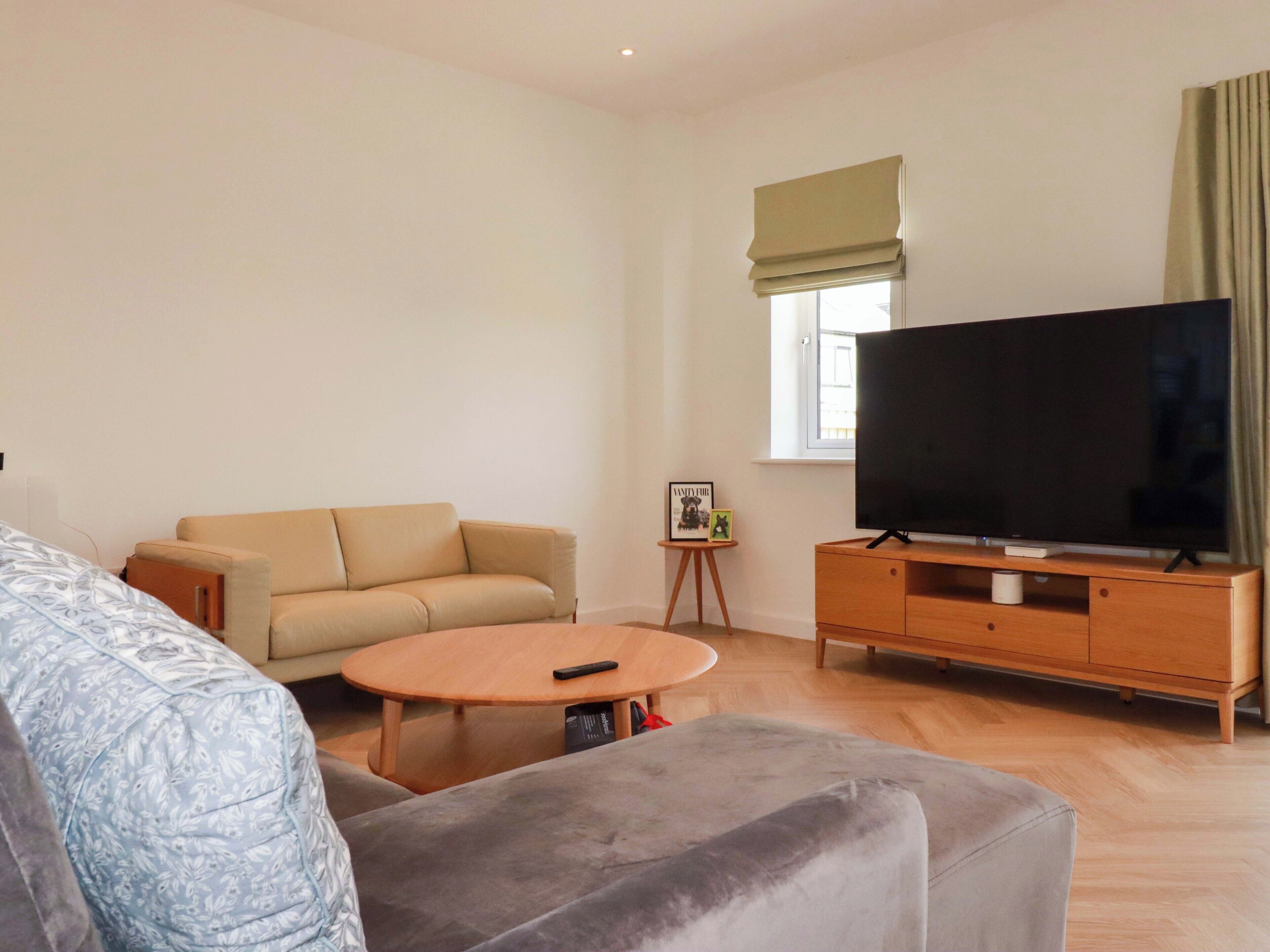 Una sala de estar con un sofá, una mesa de centro, un televisor sobre un mueble de madera y una mesita auxiliar con un marco de fotos.