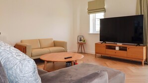 Una sala de estar con un sofá, una mesa de centro, un televisor sobre un mueble de madera y una mesita auxiliar con un marco de fotos.