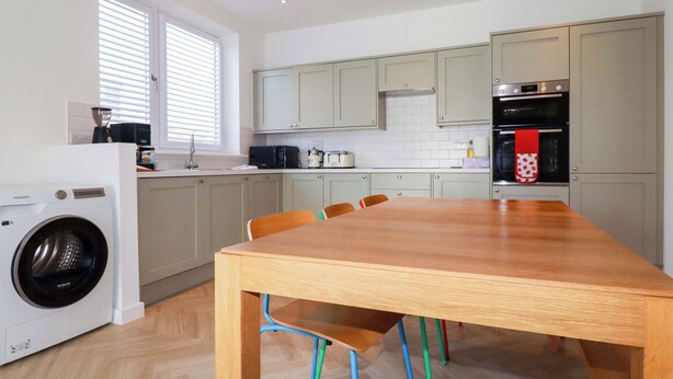 Una cocina con lavadora, una mesa de comedor con sillas y una ventana con persianas.