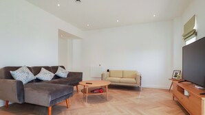 Una sala de estar moderna con un sofá gris, un sofá beige, una mesa de centro de madera y un televisor sobre un mueble de madera.