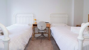 Un dormitorio con dos camas individuales, un escritorio, una silla y una mesita de noche.