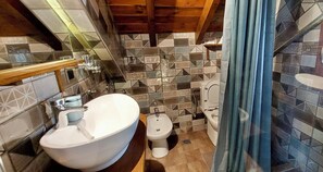 Ein Badezimmer mit einem großen weißen Waschbecken, einem Bidet und einer Toilette, mit gemusterten Fliesen an den Wänden und Holzbalken an der Decke.
