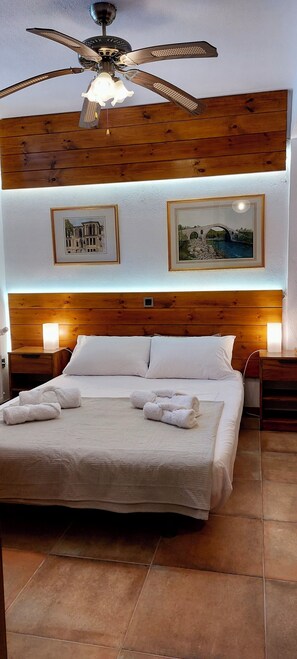 Ein Hotelzimmer mit einem großen Bett, einem hölzernen Kopfteil, zwei Wandlampen und einem Deckenventilator.