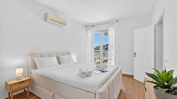 Une chambre à coucher avec un lit, une table de chevet, une lampe, des rideaux et une plante en pot.