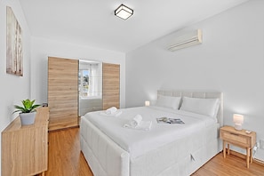 Ein modernes Schlafzimmer mit einem großen Bett, einem Nachttisch mit Lampe, einer Topfpflanze und Blick durch eine Schiebetür.