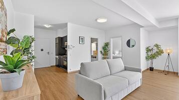 Ein modernes Wohnzimmer mit einem grauen Sofa, Holzboden und Topfpflanzen.