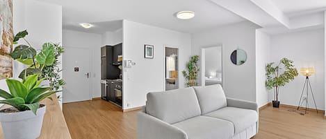 Una sala moderna con un sofá gris, suelo de madera y plantas en macetas.