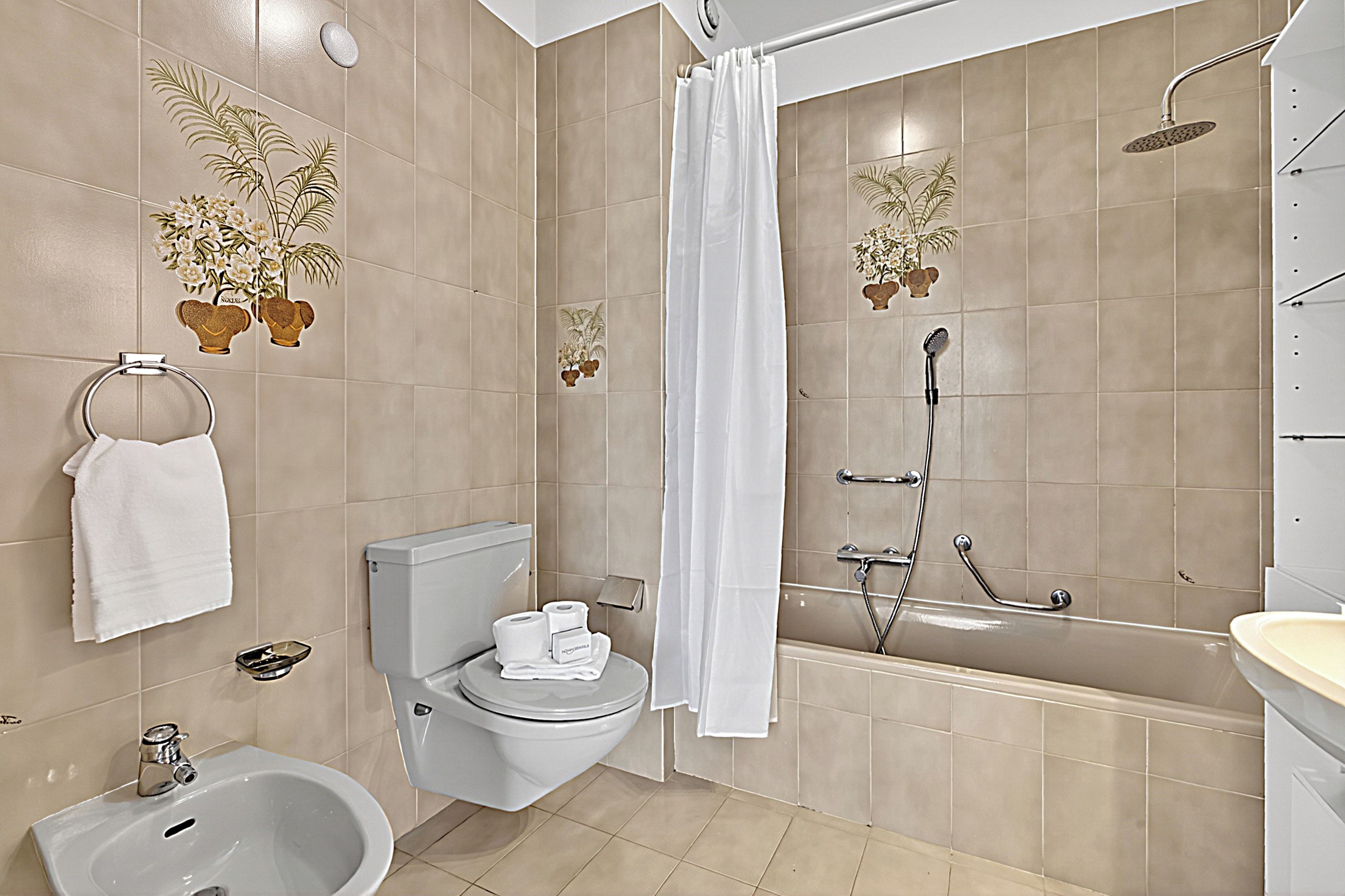 A bathroom with a toilet, bidet, sink, bathtub, shower, and decorative plants.