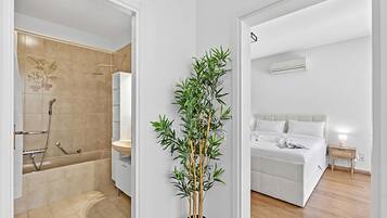Un bagno moderno con doccia, toilette e lavandino; una camera da letto con letto e comodino; e una pianta di bambù in vaso.