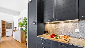 A modern kitchen with dark cabinets, a marble countertop, and a wooden cutting board with vegetables. - Lugano Sun & View Apartment for 4 (Lugano)
