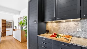 A modern kitchen with dark cabinets, a marble countertop, and a wooden cutting board with vegetables.