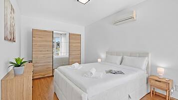 Ein modernes Schlafzimmer mit einem großen Bett, einem Nachttisch mit Lampe, einer Topfpflanze und Blick durch eine Schiebetür.