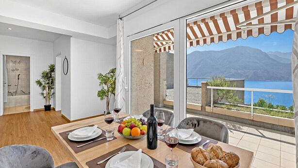 A dining area with a table set for two, a bottle of wine, fruit, and bread. - Lugano Sun & View Apartment for 4 (Lugano)