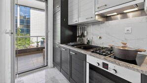 Een moderne keuken met een gasfornuis, een afzuigkap en uitzicht op een buitenbalkon via een schuifdeur.