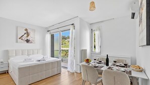 Een moderne slaapkamer met een groot bed, een eethoek met een tafel voor twee personen, en een schuifdeur naar een balkon.