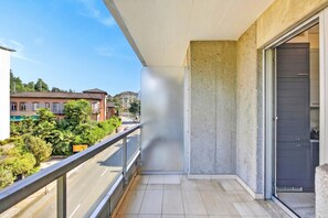 A balcony with a view of a street, a concrete wall, and a sliding glass door. - Smart Stay Lugano (Lugano)