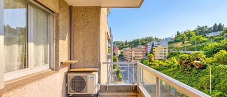 Un balcón con vistas a la ciudad, una ventana con cortinas y un equipo de aire acondicionado.