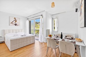 Ein modernes Schlafzimmer mit einem großen Bett, einem Essbereich mit Tisch für zwei Personen und Blick ins Freie durch eine Schiebetür.
