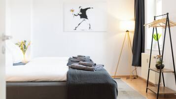 Ein ordentlich eingerichtetes Schlafzimmer mit einem Bett, einem Nachttisch mit Lampe, einem Wandbild und einem Kleiderständer.
