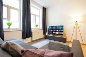 Moderni olohuone, jossa on litteänäyttöinen televisio, lattiavalaisin ja kaksi ikkunaa, joissa on verhot.