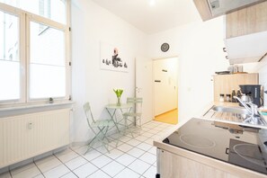 Una cocina con estufa, pileta y un pequeño comedor con sillas y mesa.