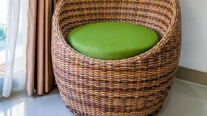 A wicker chair with a green cushion in a room with a window, curtains, and a white wall. - 2BR Villa w private Pool - Queen (Seminyak)