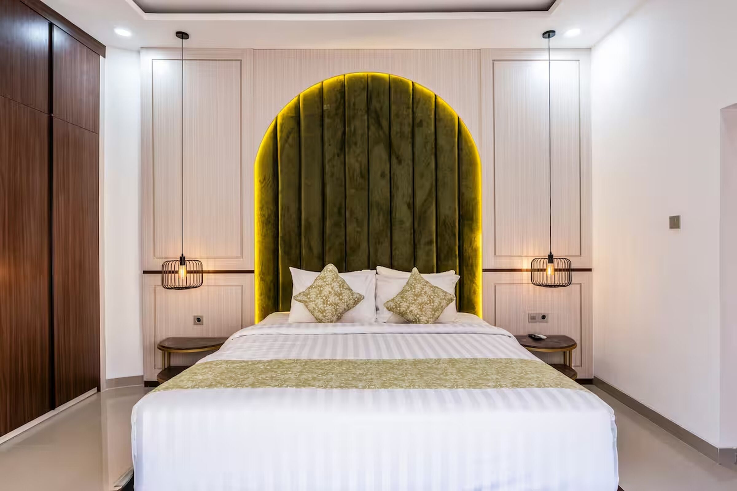 A bedroom with a large bed, two bedside tables, a green accent wall, and a wooden wardrobe.