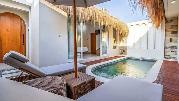 A modern outdoor pool area with lounge chairs, a thatched roof, and a stone wall. - 2BR Villa w private Pool - Queen (Seminyak)