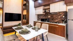 A modern kitchen with a built-in oven, microwave, and stove. There is a dining area with a table set for four. - 2BR Villa w private Pool - Queen (Seminyak)