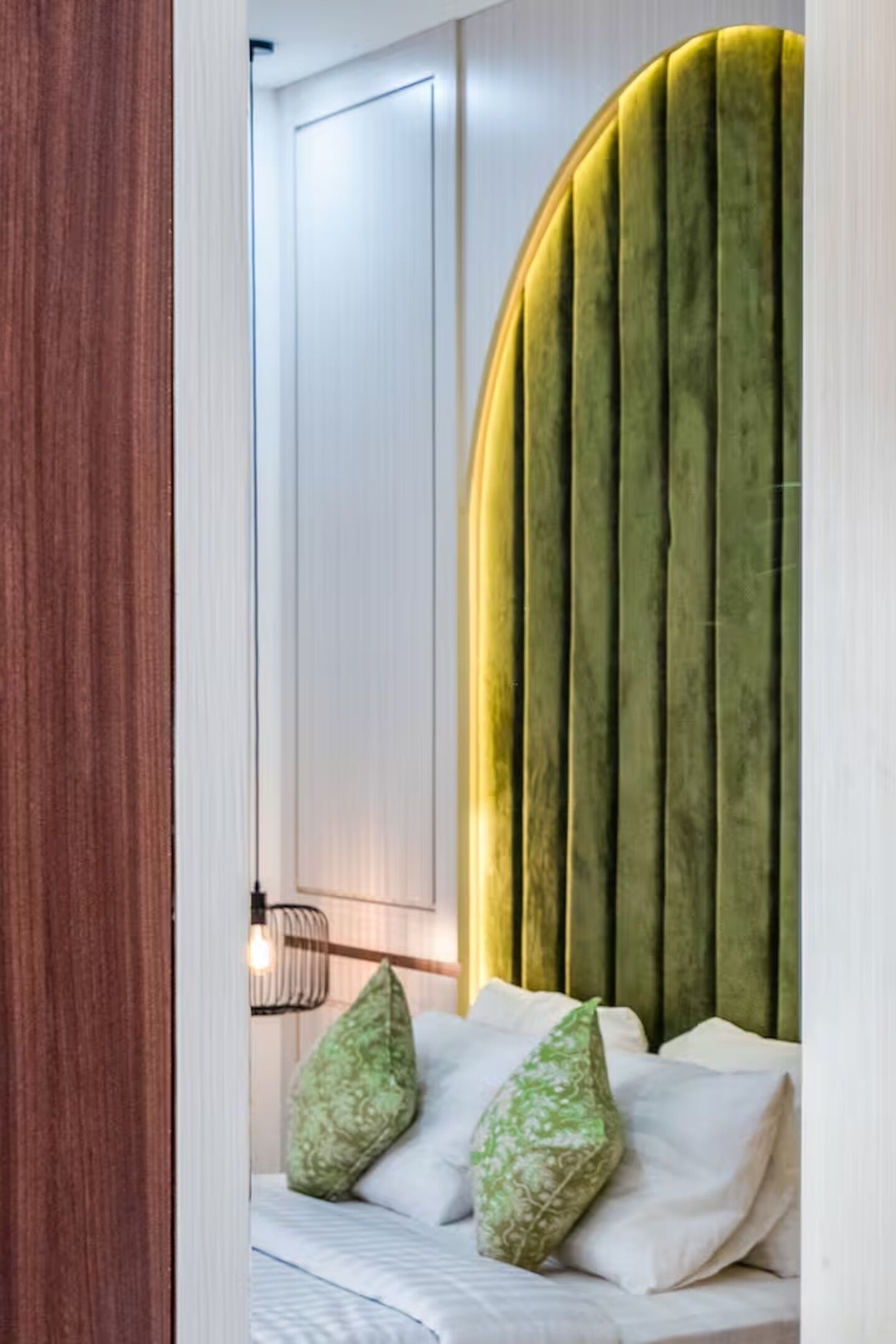 Un dormitorio con cabecera curvada, cama con ropa de cama blanca y almohada verde.