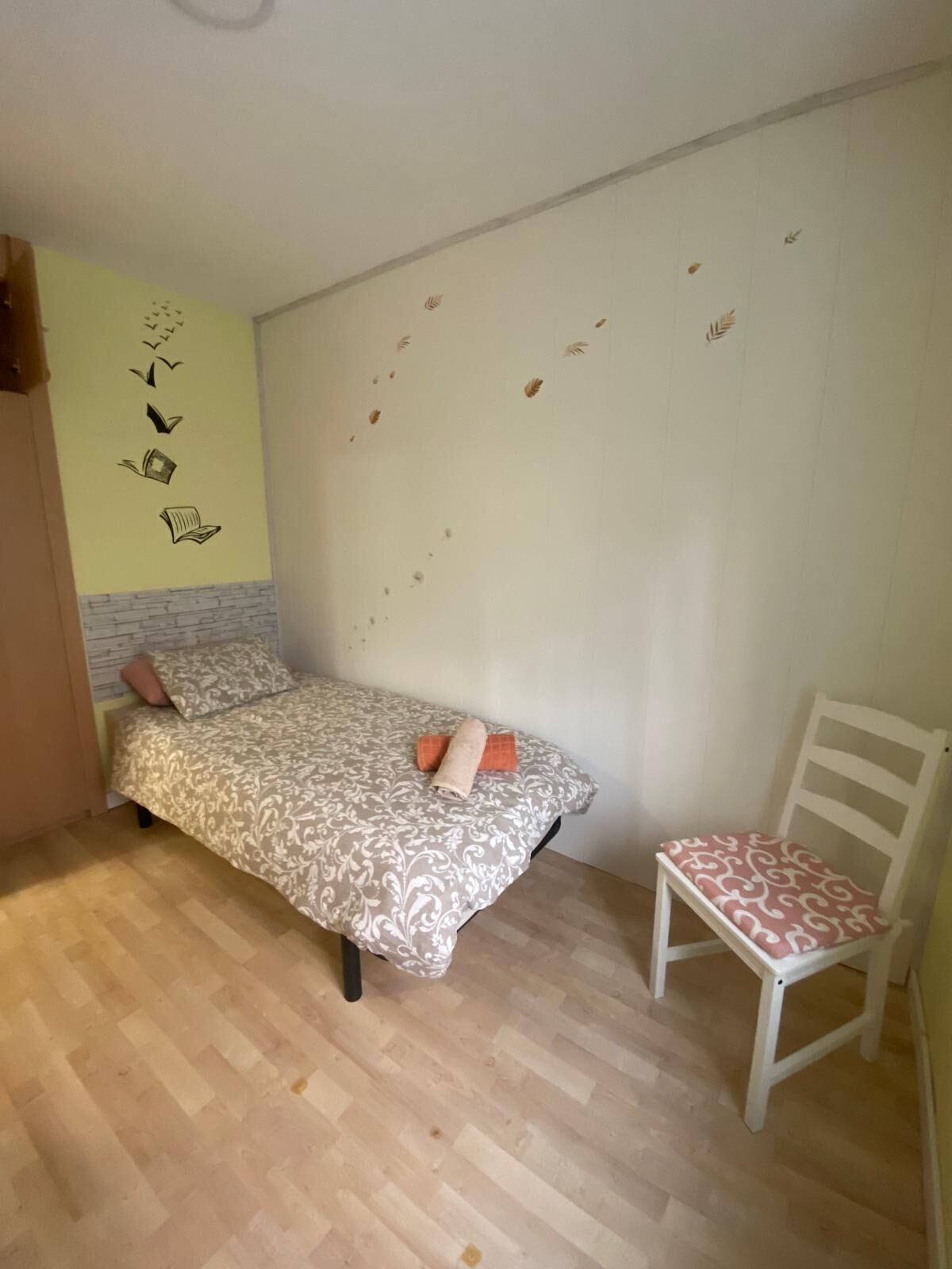 A bedroom with a bed, a chair, and a wall with leaf patterns.