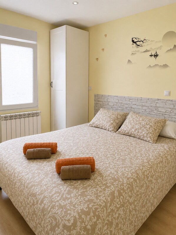 A bedroom with a bed, pillows, a radiator, a wardrobe, and a wall with a landscape painting. - Dreams Home Burgos - Complete and quiet apartment 2 minutes from downtown (Burgos)