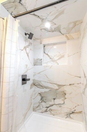 Une salle de bain avec des murs en marbre, une douche et une baignoire.