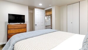 Un dormitorio con cama, televisor en una cómoda, armario y puerta que da a un baño.