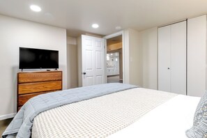 Ein Schlafzimmer mit einem Bett, einem Fernseher auf einer Kommode, einem Kleiderschrank und einer Tür zu einem Badezimmer.