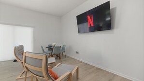 A modern living room with a flat-screen TV, wooden chairs, a dining table, and a grey sofa. - Garage Studio King + Queen Studio | Private Patio (Smithfield)
