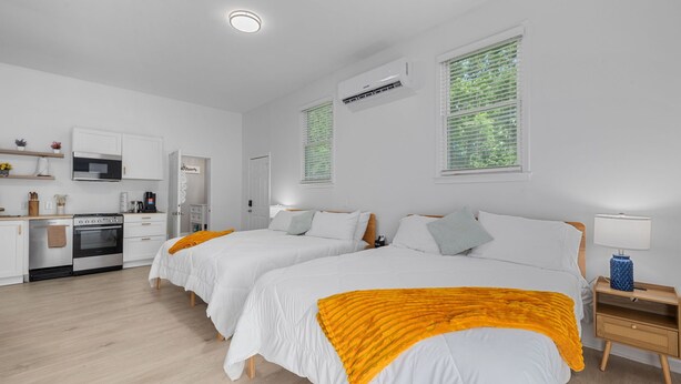 A modern hotel room with two beds, a kitchenette, and a bathroom. - Garage Studio King + Queen Studio | Private Patio (Smithfield)