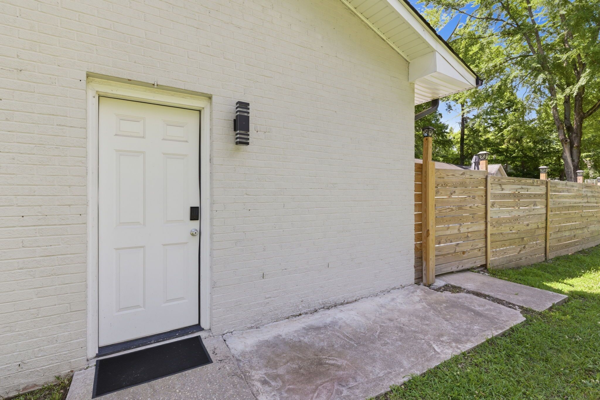 A white brick building with a white door, a small black mailbox, and a wooden fence.