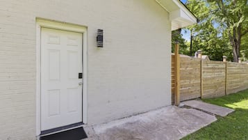 A white brick building with a white door, a small black mailbox, and a wooden fence.