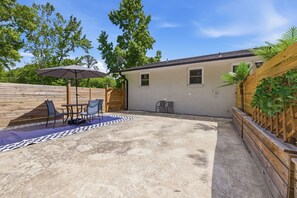 Un patio techado con mesa y sillas, una cerca de madera y un edificio pequeño.
