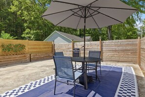 Eine Terrasse im Freien mit Tisch, Stühlen, einem großen Sonnenschirm und einem karierten Teppich.