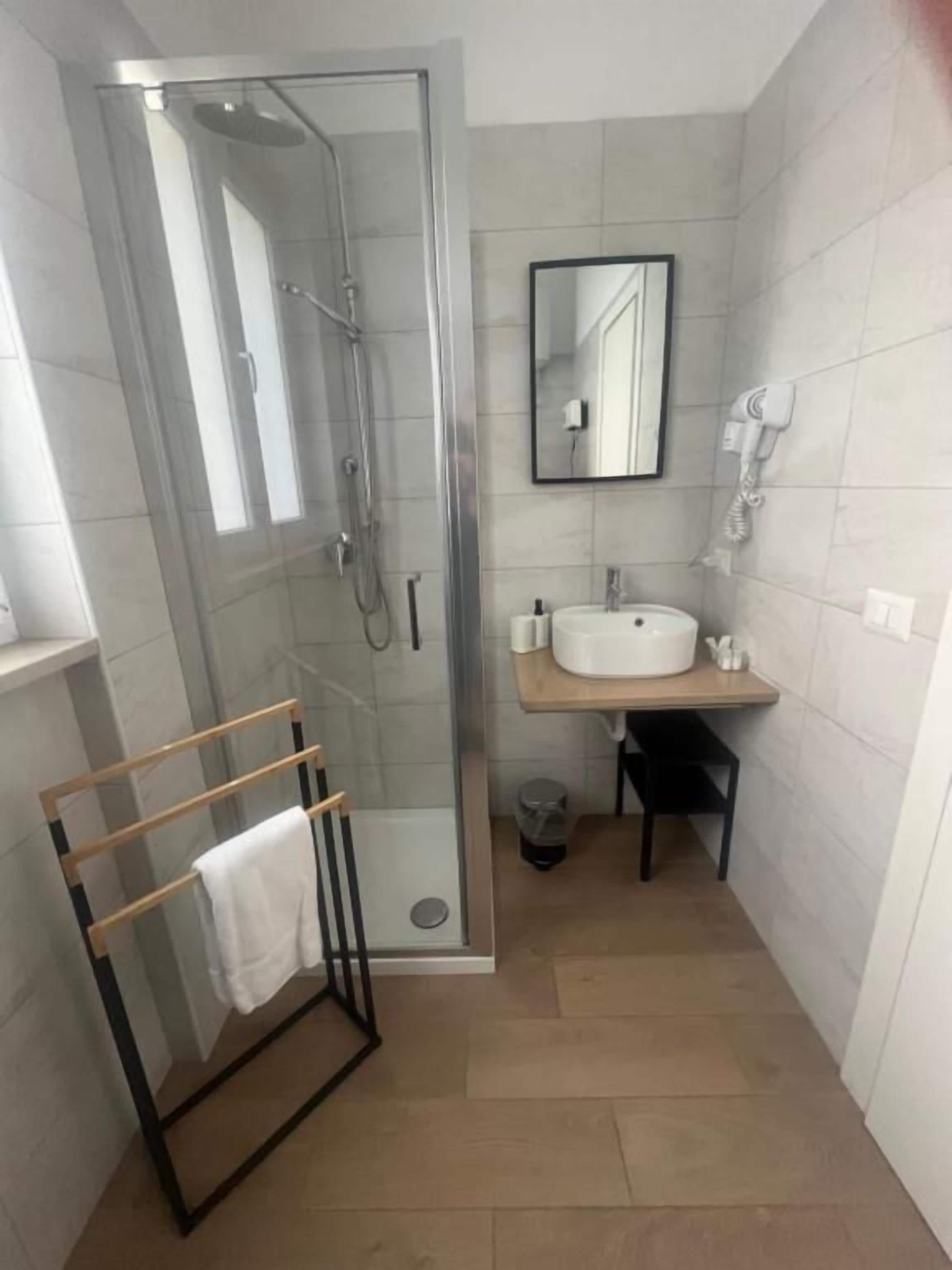 Un baño pequeño con cabina de ducha de vidrio, un lavabo blanco, un espejo y un perchero para toallas.