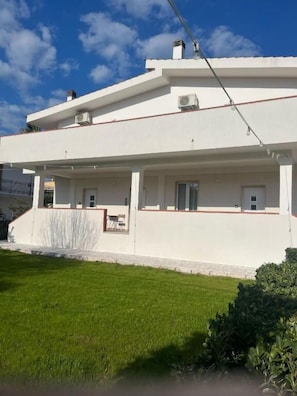 A two-story building with a flat roof, air conditioning units, and a small balcony.