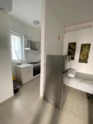 Eine Küche mit Kühlschrank, weißen Schränken, einem Fenster und Bildern an der Wand.