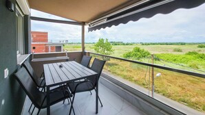 Een balkon met een tafel en stoelen, uitzicht op een bakstenen gebouw en een grasveld.