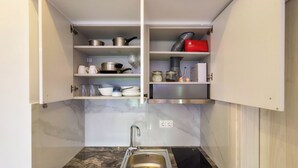 Een keuken met een spoelbak, fornuis en kastjes met pannen, potten en potten.