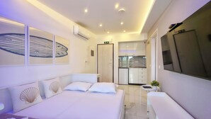 Een moderne hotelkamer met een bed, een kleine kitchenette en een aan de muur bevestigde televisie.