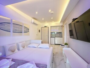 A modern hotel room with a bed, a small kitchenette, and a TV mounted on the wall. - 19 - IFESTOS Suites by SDR (Paralia)