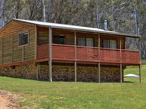 A log cabin with a stone foundation, a balcony, and a chimney. - Your gateway to an unforgettable holiday experience in the stunning Snowy Mountains! (Adaminaby)