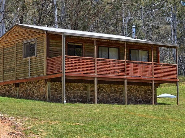 A log cabin with a stone foundation, a balcony, and a chimney.